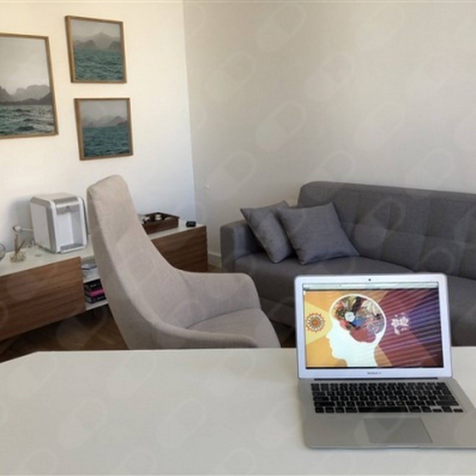 A sala de atendimento: sofá em tom taupe, poltrona clara e quadros de mar na parede.